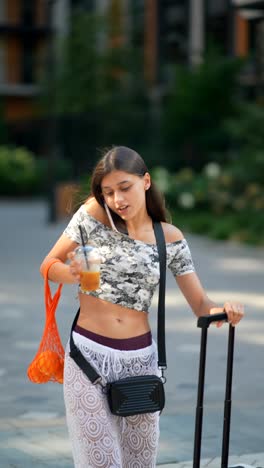 young woman traveling in city with drink and luggage