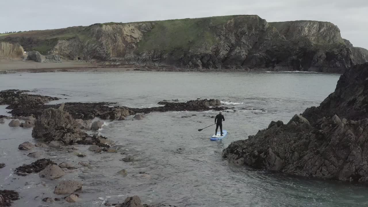 hombre rema sup paddleboard a través de peligrosas rocas oceánicas cerca de la costa