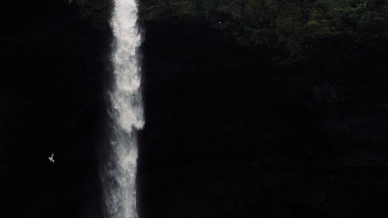 tomas en cámara lenta de una remota cascada islandesa con un hombre caminando hacia ella
