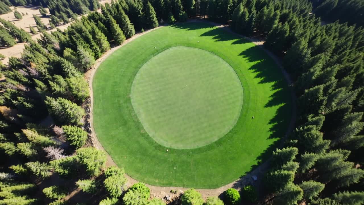 Drone che scende ruotando sopra un green da golf nella foresta, rivelando una superficie di putting chiara e segnaposto bianchi.