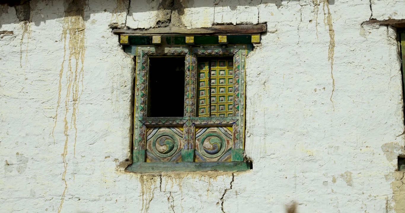 Annapurna Çevresi, Mustang, Nepal: Geleneksel bir köy evinin yıpranmış, badanalı kerpiç duvarında çerçevelenmiş süslü, el oyması ahşap bir pencere.