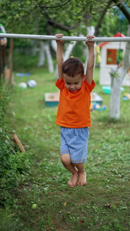 beautiful caucasian kid training on the horizontal bar. toddler doing sport since early age. garden at backdrop. vertical video.