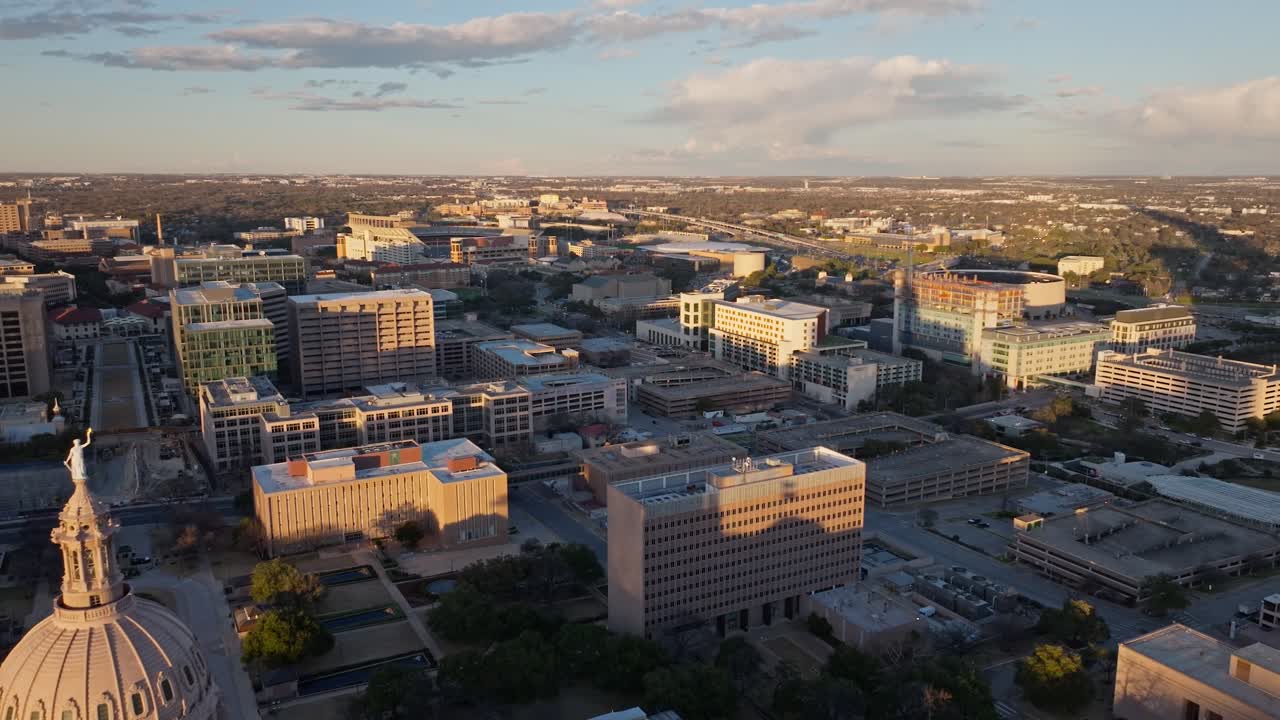 A drone flyby of the domed Texas State Capitol Building in Austin at sunset with long shadows and the Goddess of Liberty statue heading towards the University of Texas stadium