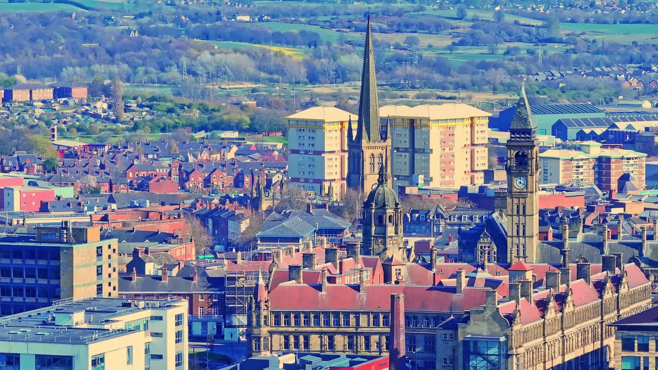 Aerial view ascending over Wakefield’s cathedral, All Saints Church, revealing detailed stone architecture, traditional brick houses, and surrounding greenery in the historic Yorkshire town. England.