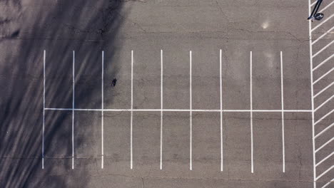 una toma de ángulo alto de arriba hacia abajo directamente sobre un estacionamiento vacío con un hombre jugando con un automóvil eléctrico con control remoto