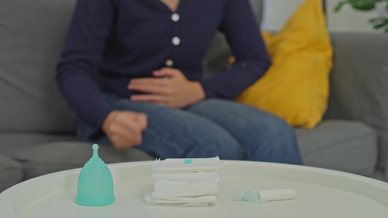 Woman holding her belly in pain during menstruation with period protection products on table
