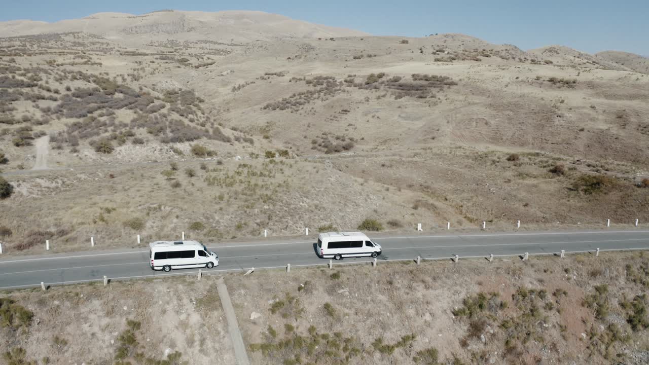 una amplia toma aérea de dos minibuses blancos a alta velocidad moviéndose en la carretera armenia llena de turistas en la provincia de kotayk