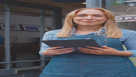 vertical video portrait of female owner or staff standing outside coffee shop with digital tablet