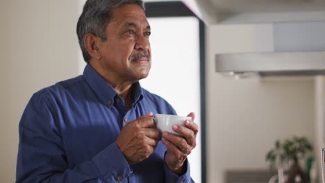 Senior-mixed-race-man-in-kitchen-drinking-coffee