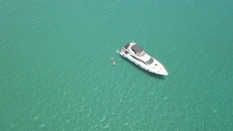 drone rising high from beautiful white yacht, people swimming beside, cyprus