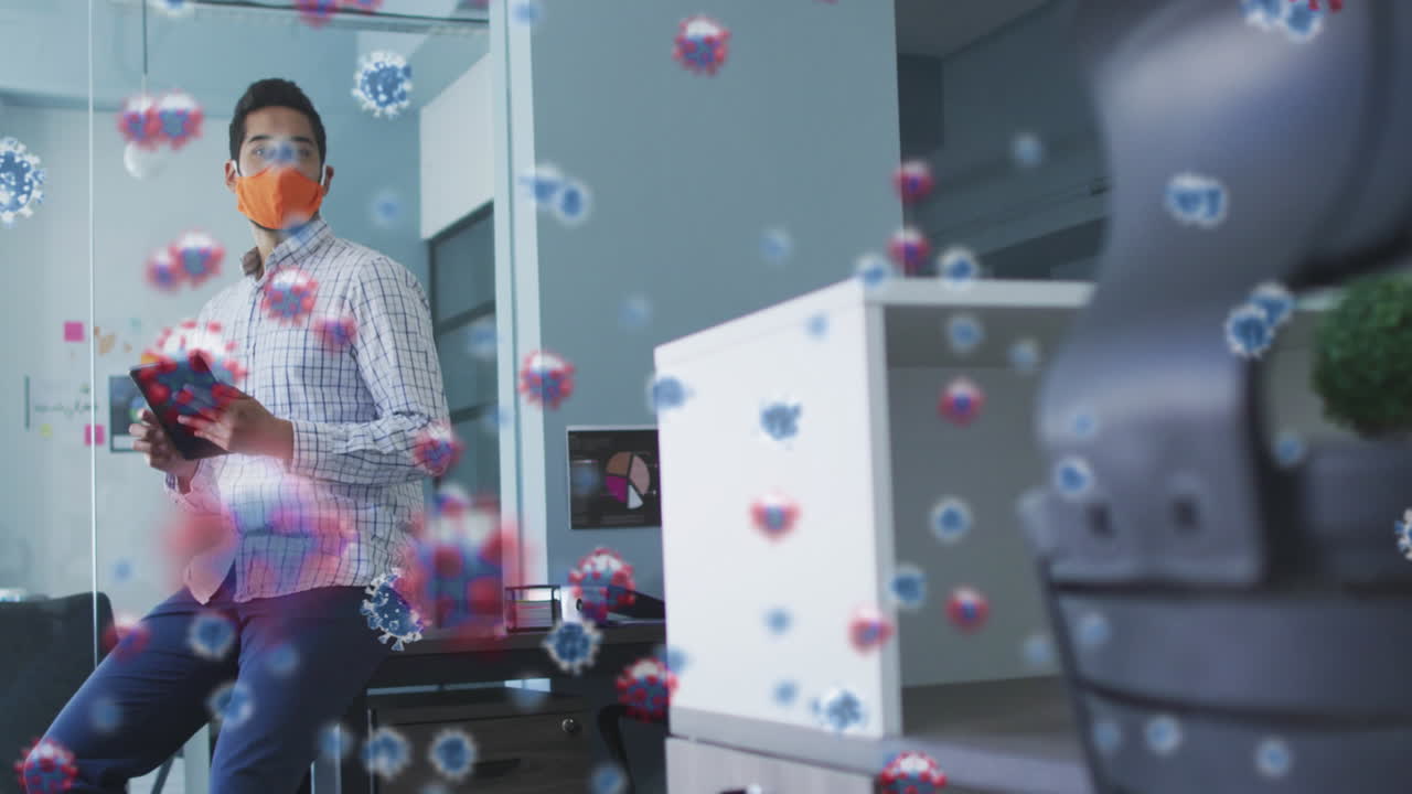 사무실에서 디지털 태블릿을 사용하여 얼굴 마스크를 착용한 남성에 대해 여러 개의 코로나 19가 떠다니고 있습니다.