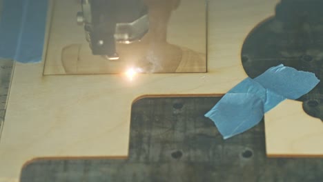 a laser engraver etching the frame around a portrait that has been engraved into wood on a workbench