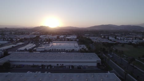 a drone glides effortlessly over a captivating scene, capturing both commercial warehouses and a serene park, bathed in the golden glow of a sunset