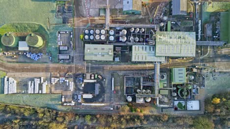 Direct-overhead-aerial-footage-of-a-large-industrial-plant-showing-pipework-structures,-buildings,-cooling-towers,-steam,-and-work-vehicles