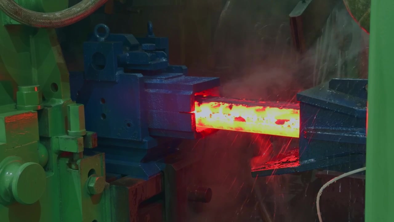 Close-up of glowing red hot steel rebar moving through heavy machinery with steam in industrial manufacturing plant