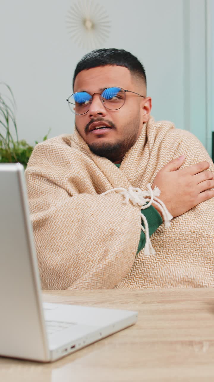 Sick ill indian man freelancer working on laptop wrapped in plaid sit shivering from cold at home