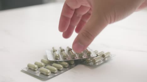 Person-picking-up-various-pills-on-a-table