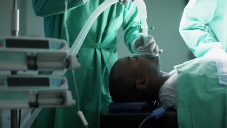 surgeon using anaesthetic mask on african american male patient in operating theatre, slow motion