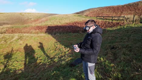 Un-Niño-Y-Su-Madre-Afuera-En-El-Campo,-Volando-Su-Dron-FPV-Con-Un-Casco-De-Realidad-Virtual-Y-Practicando-Sus-Habilidades-Deportivas.