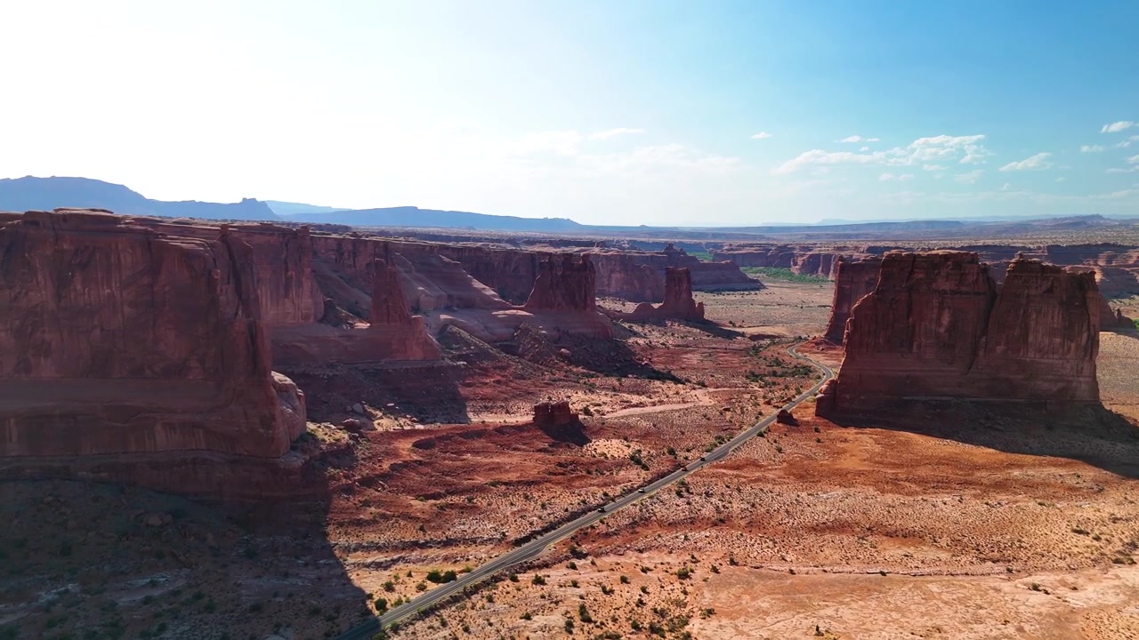 Splendido filmato stock del Parco Nazionale di Arches, USA, durante un pomeriggio luminoso. La luce solare brillante illumina le maestose strutture di arenaria rossa e il paesaggio desertico sotto un cielo azzurro limpido.