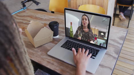 mujer tomando un bocadillo mientras hace una videollamada en una computadora portátil en una cafetería