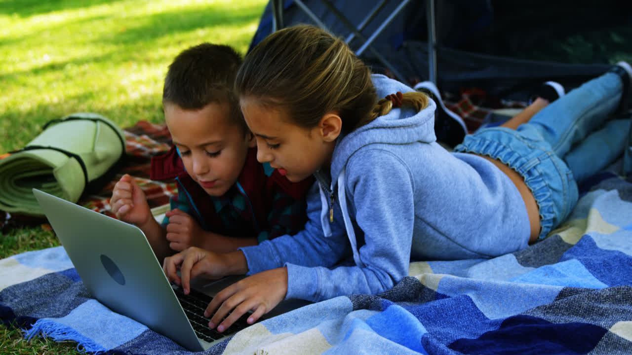 hermanos usando computadora portátil fuera de la tienda en el campamento