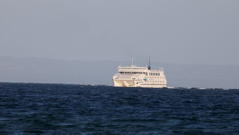 a ferry travels across calm ocean waters under clear skies, captured in steady daylight with a serene atmosphere