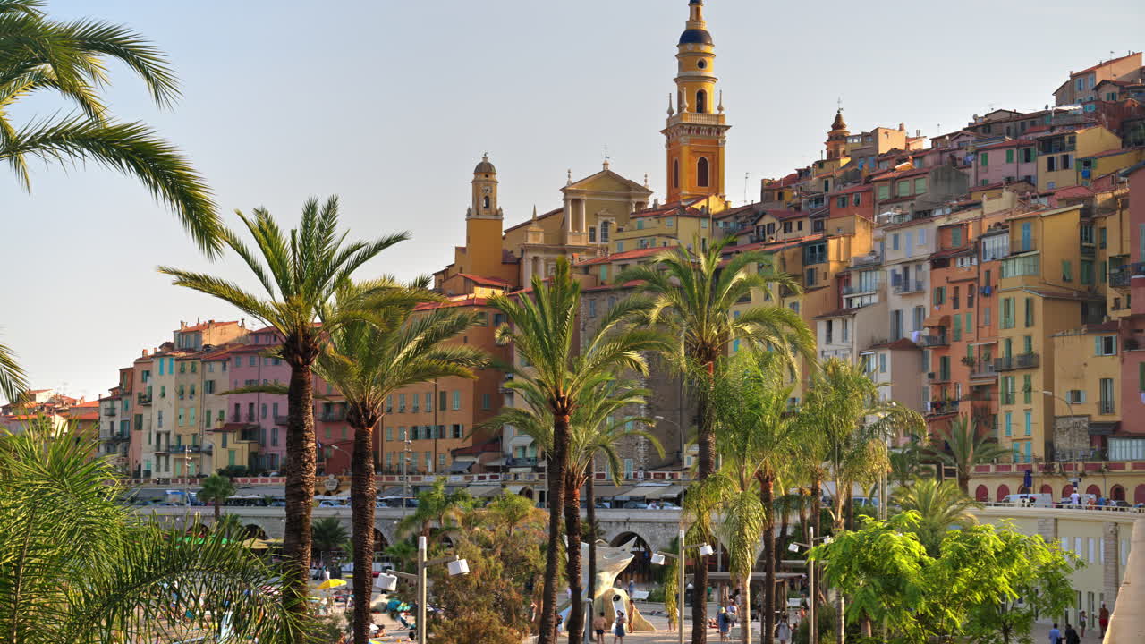 View of palm trees with the colourful buildings in Menton, France on the background