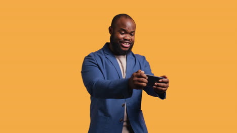 happy man playing videogames on smartphone, celebrating, studio background