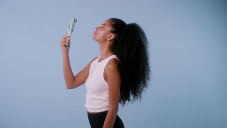 cheerful model with dark curly hair and brown skin cools herself with a mini fan and smiles joyfully.