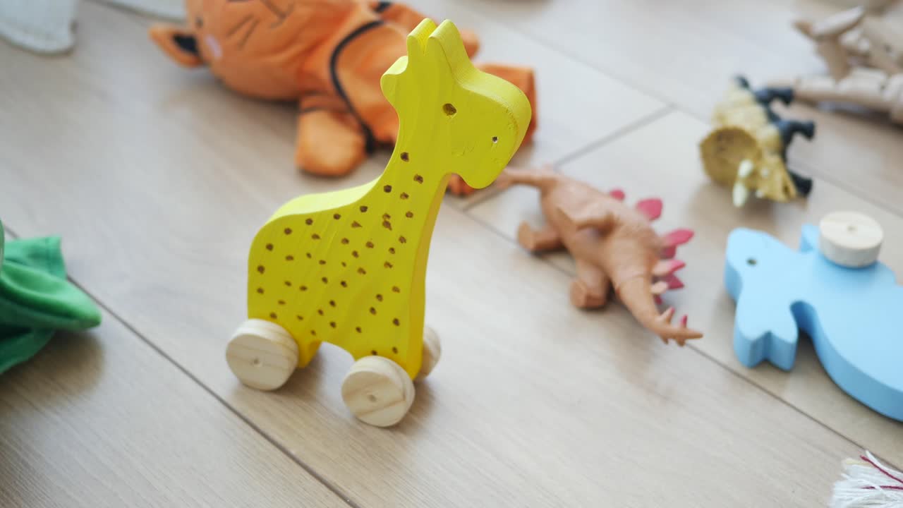 A yellow wooden giraffe toy and other children's toys on a light wooden floor