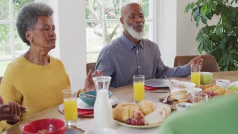 Video-Von-Glücklichen-Afroamerikanischen-Großeltern,-Die-Händchen-Halten-Und-Mit-Der-Familie-Am-Esstisch-Gnade-Sagen