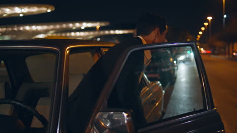 man driver opening car door going night street. businessman closed automobile