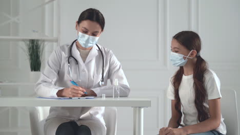 young pretty female doctor and little girl patient with a face mask at the office