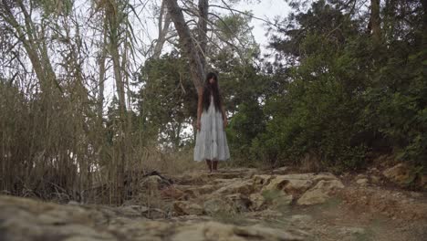 a women in white dress is walking barefood in the forest