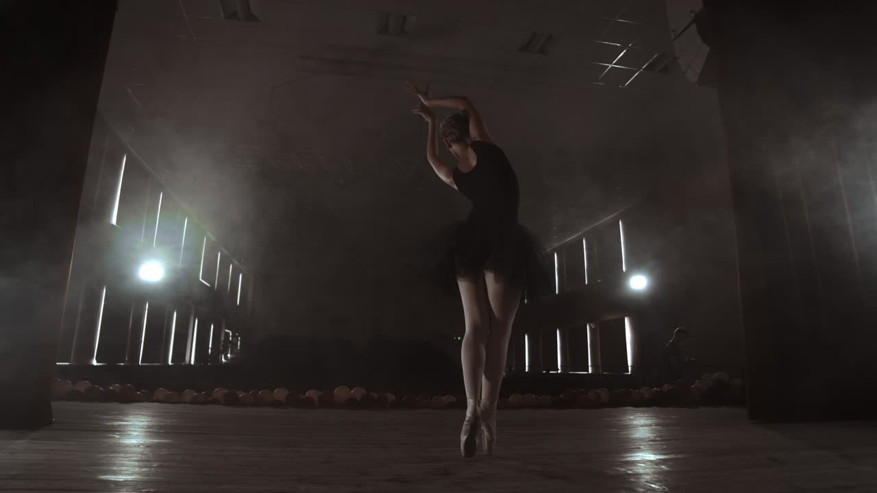 Slow motion: prima ballet in a black dress performs rotations and dance graceful movements rehearsing a solo program. The camera moves on gimbal