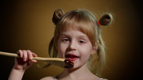 playful teen child kid girl eating, licking melted chocolate sweet candy syrup from wooden spoon