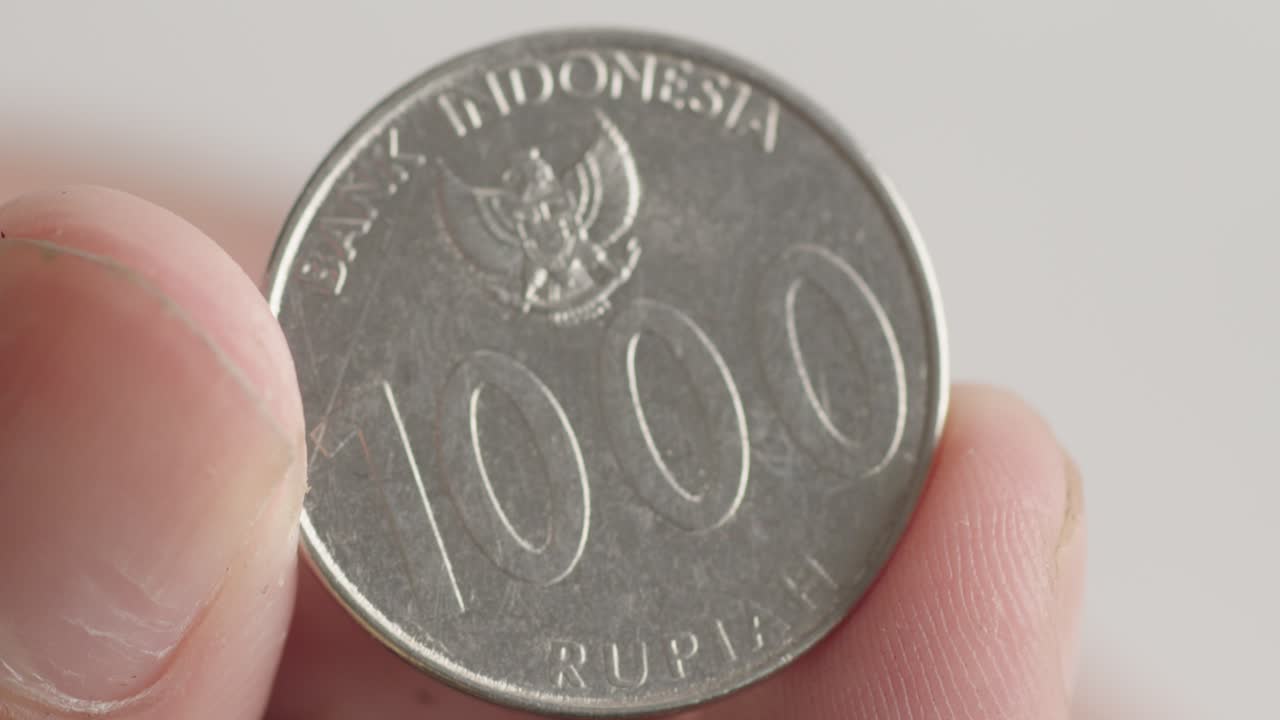 sosteniendo entre los dedos una moneda de 1000 rupias indonesias