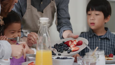 happy asian family eating pancakes for breakfast children enjoying healthy homemade meal with parents on weekend morning in kitchen 4k footage