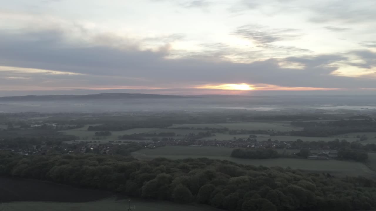 Drone aerial view above British rural farm countryside broadcast signal towers at sunrise rising pan left