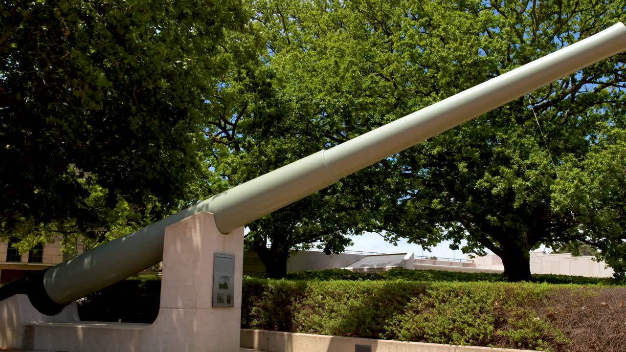 Un’ampia inquadratura statica di un enorme cannone storico con canna rivolta verso lussureggianti alberi verdi all'aperto