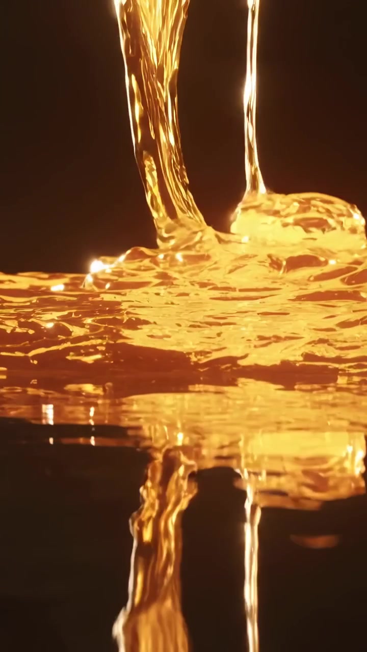 Corong di luar bingkai menuangkan minyak kuning kemerahan, membentuk riak di kolam cermin di studio gelap, menunjukkan kilau hangat.