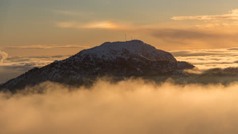 inversion clouds surrounding snow capped mountain løvstakken in bergen, norway