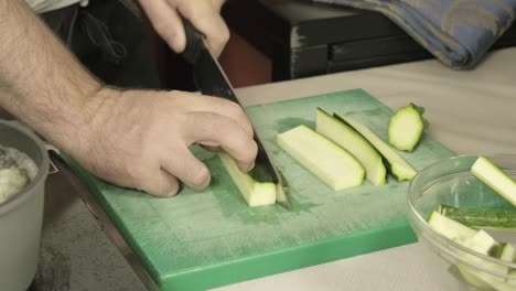 Hands-cut-a-green-zucchini-in-kitchen-with-boiling-water-close-up,-sharp-knife