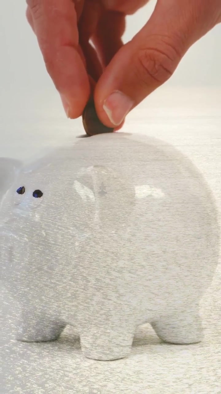 Vertical video: Hand entering with coin, lowering pressing coin into piggy bank slot to save
