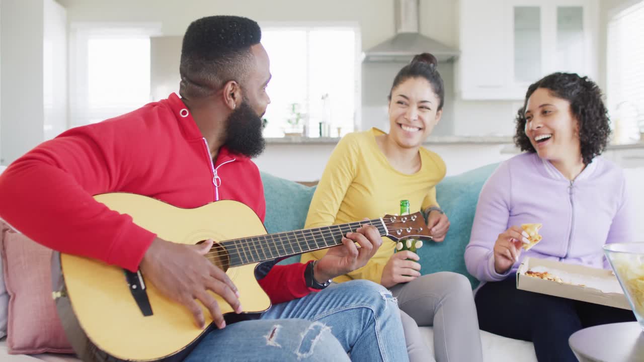 Amici e amiche felici di diverse provenienze che suonano la chitarra e ascoltano a casa, al rallentatore.