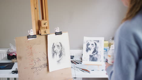 Female-Teenage-Artist-Spraying-Lacquer-Fixative-Onto-Drawing-Picture-Of-Dog-In-Charcoal