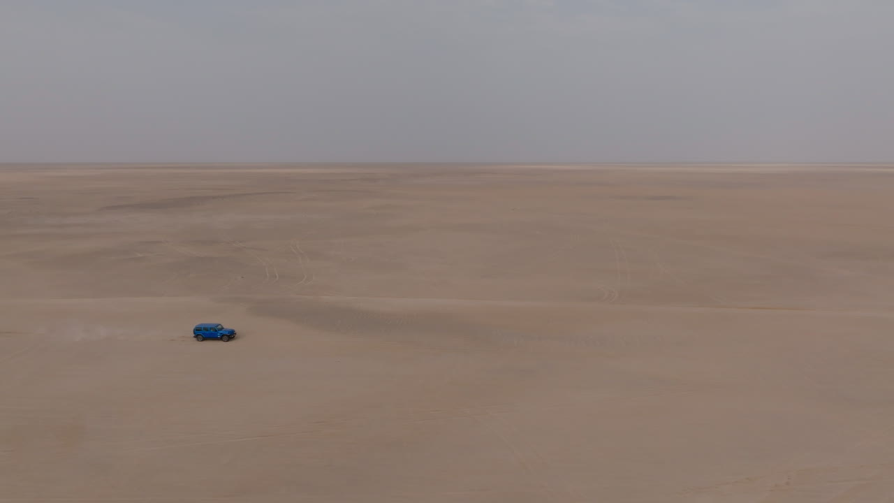 Blue truck drives alone through vast desert plain on road to Bar al Hikman, Oman