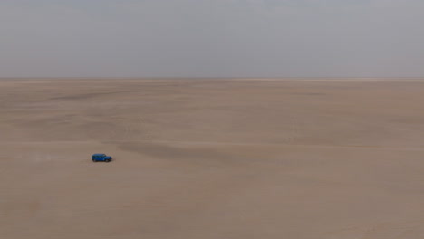 blue truck drives alone through vast desert plain on road to bar al hikman, oman