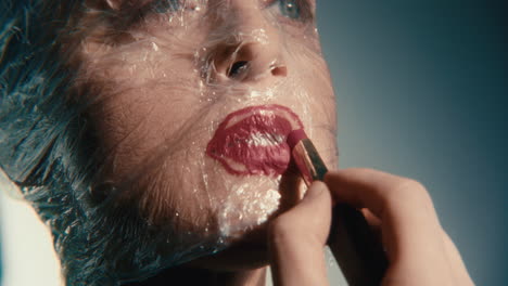 woman with plastic face wrapped getting lipstick applied
